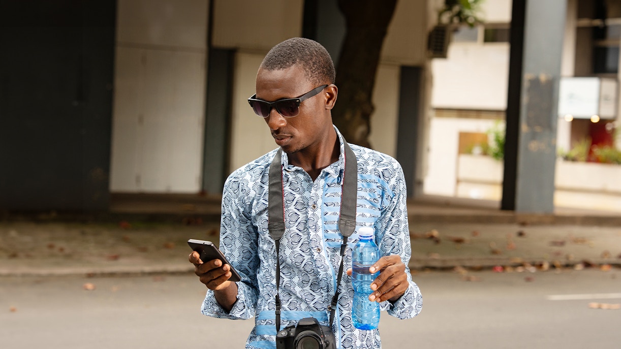 Tourist holding a camera and water bottle in a sunny outdoor setting.