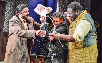Actors in a comedic scene from "The Play That Goes Wrong" with water being poured.