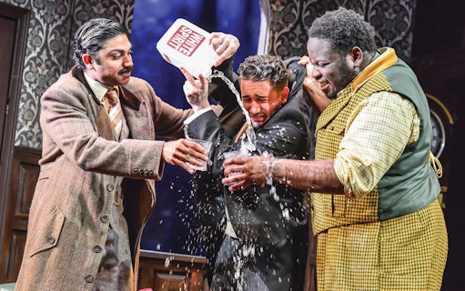 Actors in a comedic scene from "The Play That Goes Wrong" with water being poured.