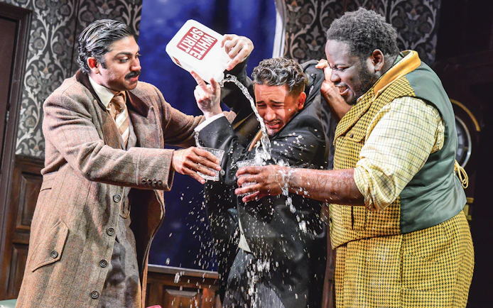 Actors in a comedic scene from "The Play That Goes Wrong" with water being poured.