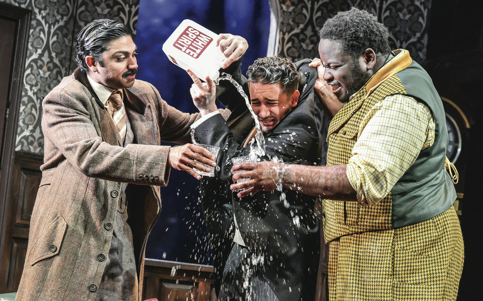 Actors in a comedic scene from "The Play That Goes Wrong" with water being poured.