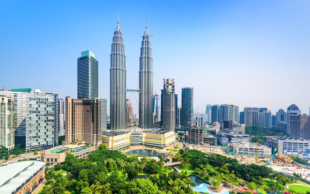Petronas Twin Towers in Kuala Lumpur, Malaysia, surrounded by city skyline and lush park.