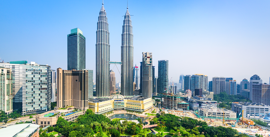 Petronas Twin Towers in Kuala Lumpur, Malaysia, surrounded by city skyline and lush park.