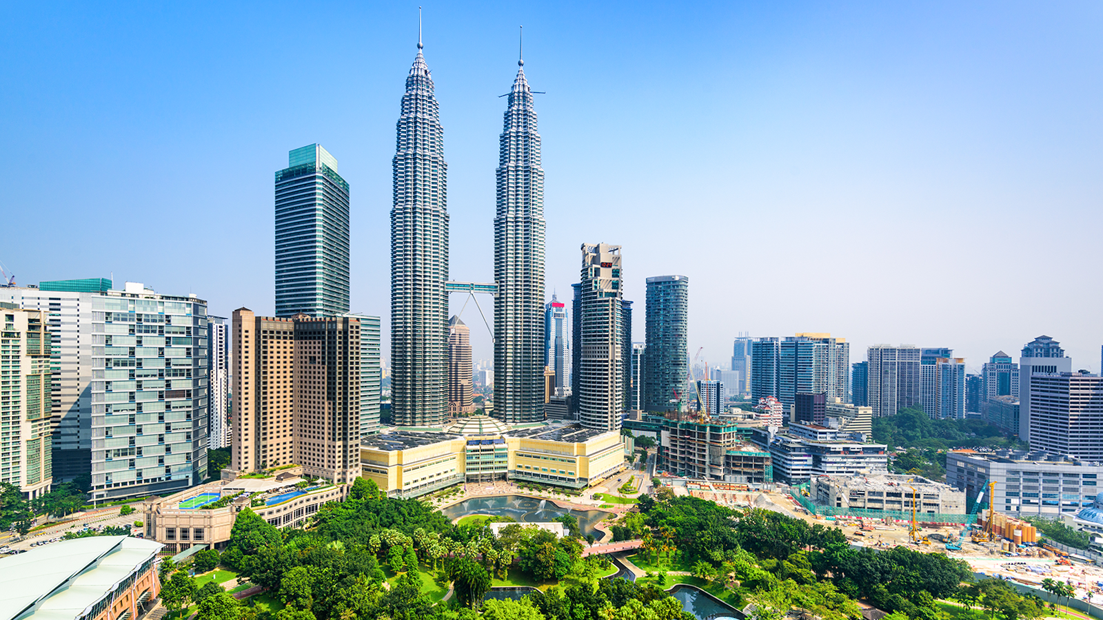 Petronas Twin Towers in Kuala Lumpur, Malaysia, surrounded by city skyline and lush park.