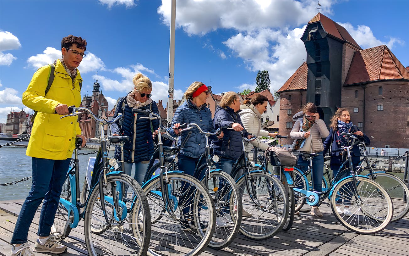 Group of cyclists on a Gdansk bike tour near historic waterfront buildings.