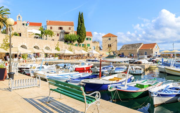 Boats docked at Bol Town harbor on Brac Island, Croatia, with stone buildings in the background.