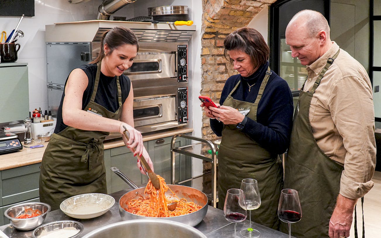 Participants in a pasta making class cooking spaghetti in a kitchen setting.