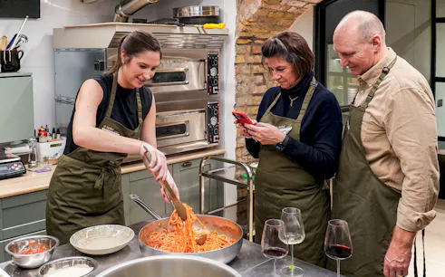 Participants in a pasta making class cooking spaghetti in a kitchen setting.