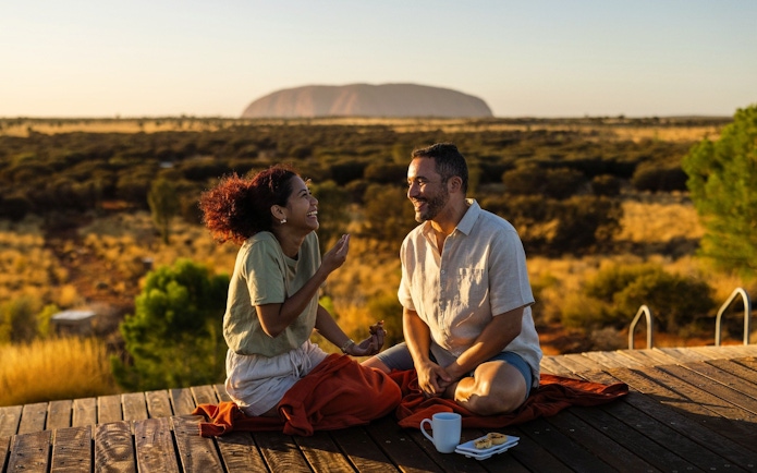Couple enjoying breakfast with view of Uluru during Outback camping adventure.