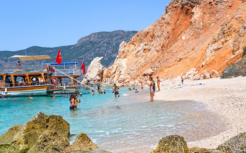 Boat anchored near Suluada Island beach with people swimming, Antalya day trip.