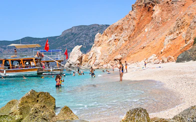 Boat anchored near Suluada Island beach with people swimming, Antalya day trip.