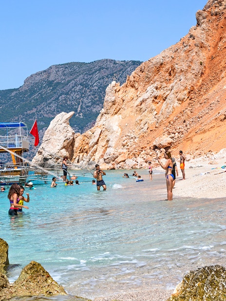 Boat anchored near Suluada Island beach with people swimming, Antalya day trip.