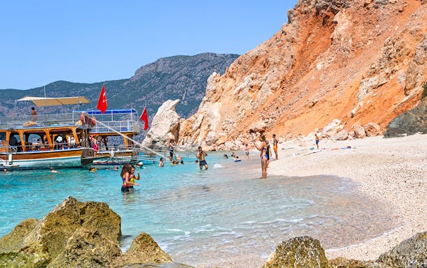 Boat anchored near Suluada Island beach with people swimming, Antalya day trip.