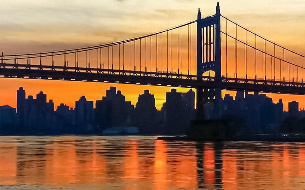 Sunset view of New York City skyline and bridge from Statue of Liberty cruise.