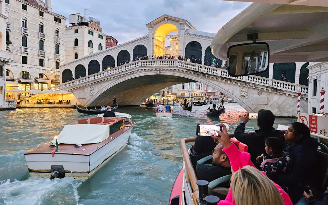 Vaporetto ACTV water bus passing under Rialto Bridge in Venice with tourists onboard.