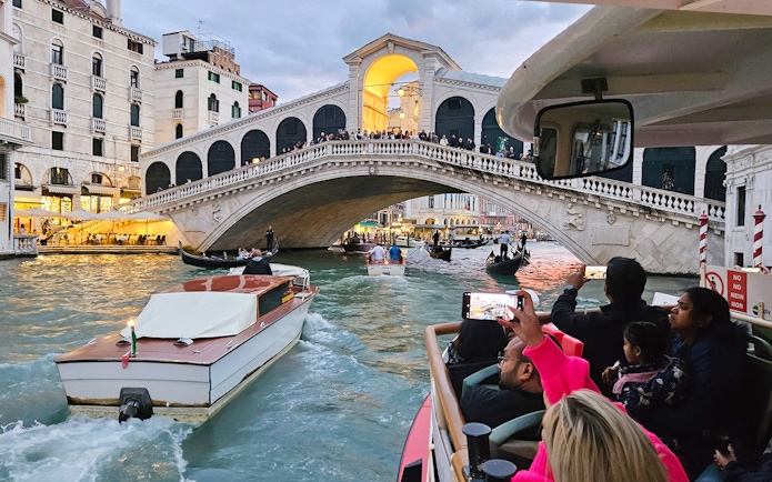 Vaporetto ACTV water bus passing under Rialto Bridge in Venice with tourists onboard.