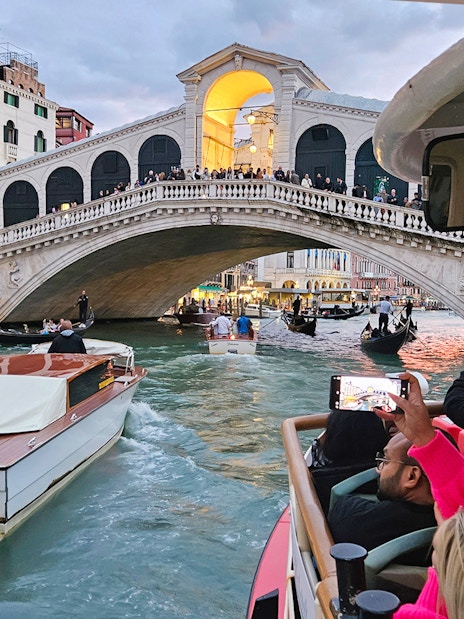 Vaporetto ACTV water bus passing under Rialto Bridge in Venice with tourists onboard.