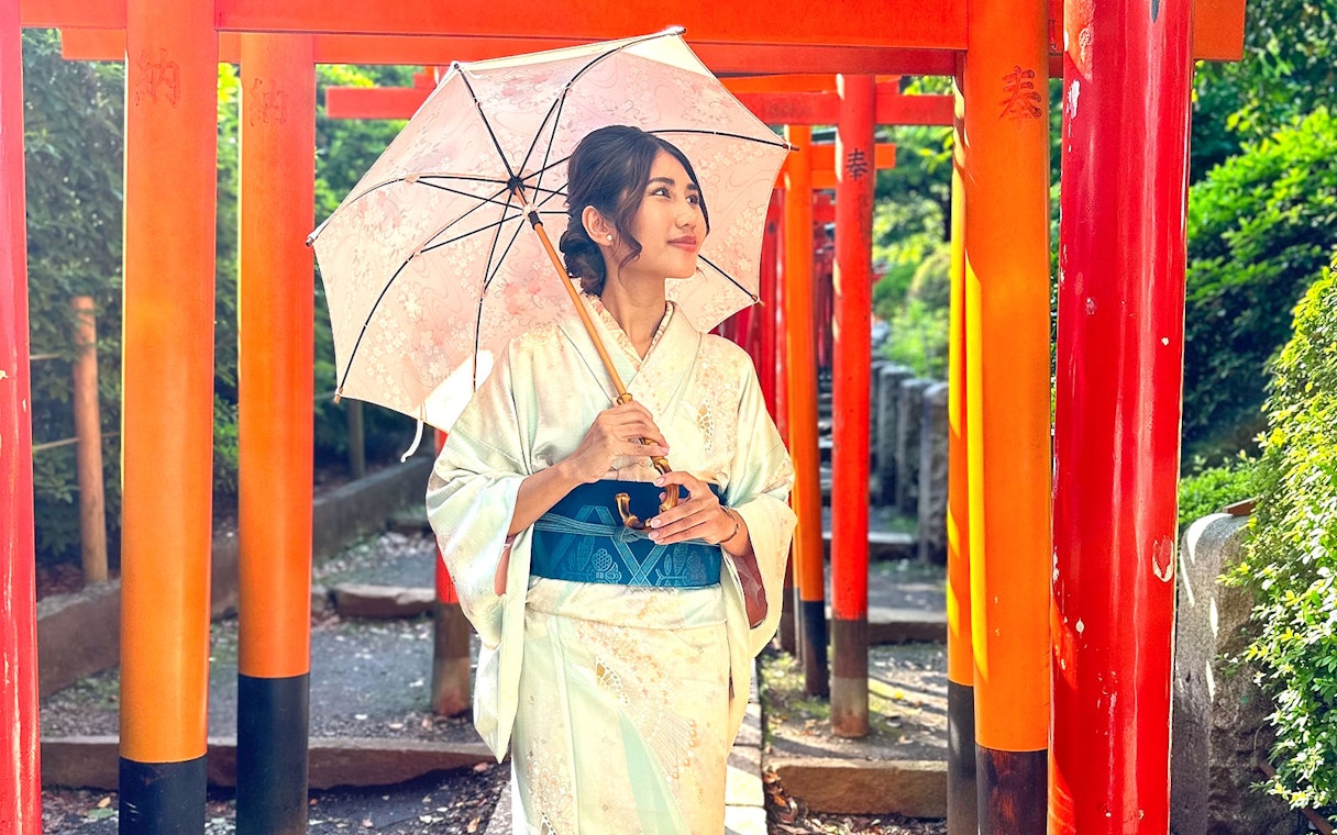 Woman in kimono holding umbrella, standing among red torii gates in Shinagawa, Tokyo.