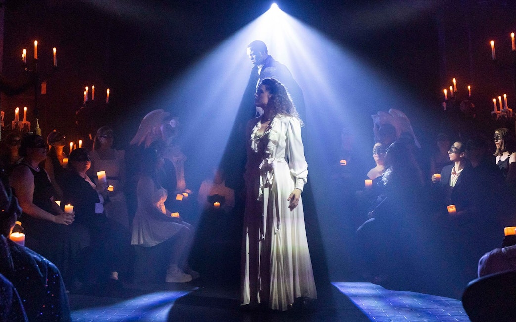 Masquerade Broadway stage performance with actors in spotlight and audience holding candles.