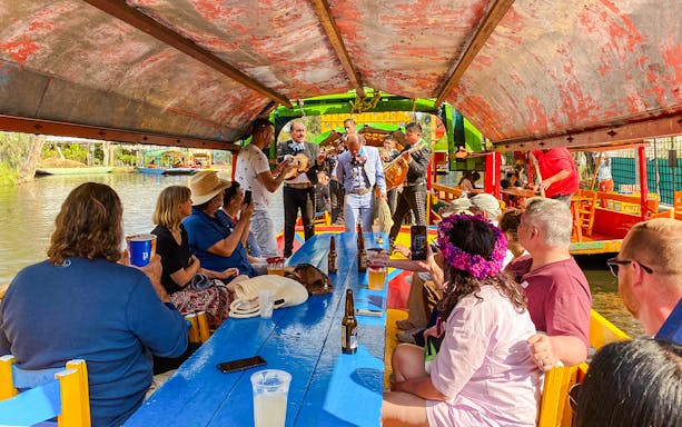 Colorful trajinera boats on Xochimilco canal, Mexico City, with tourists enjoying a guided tour.