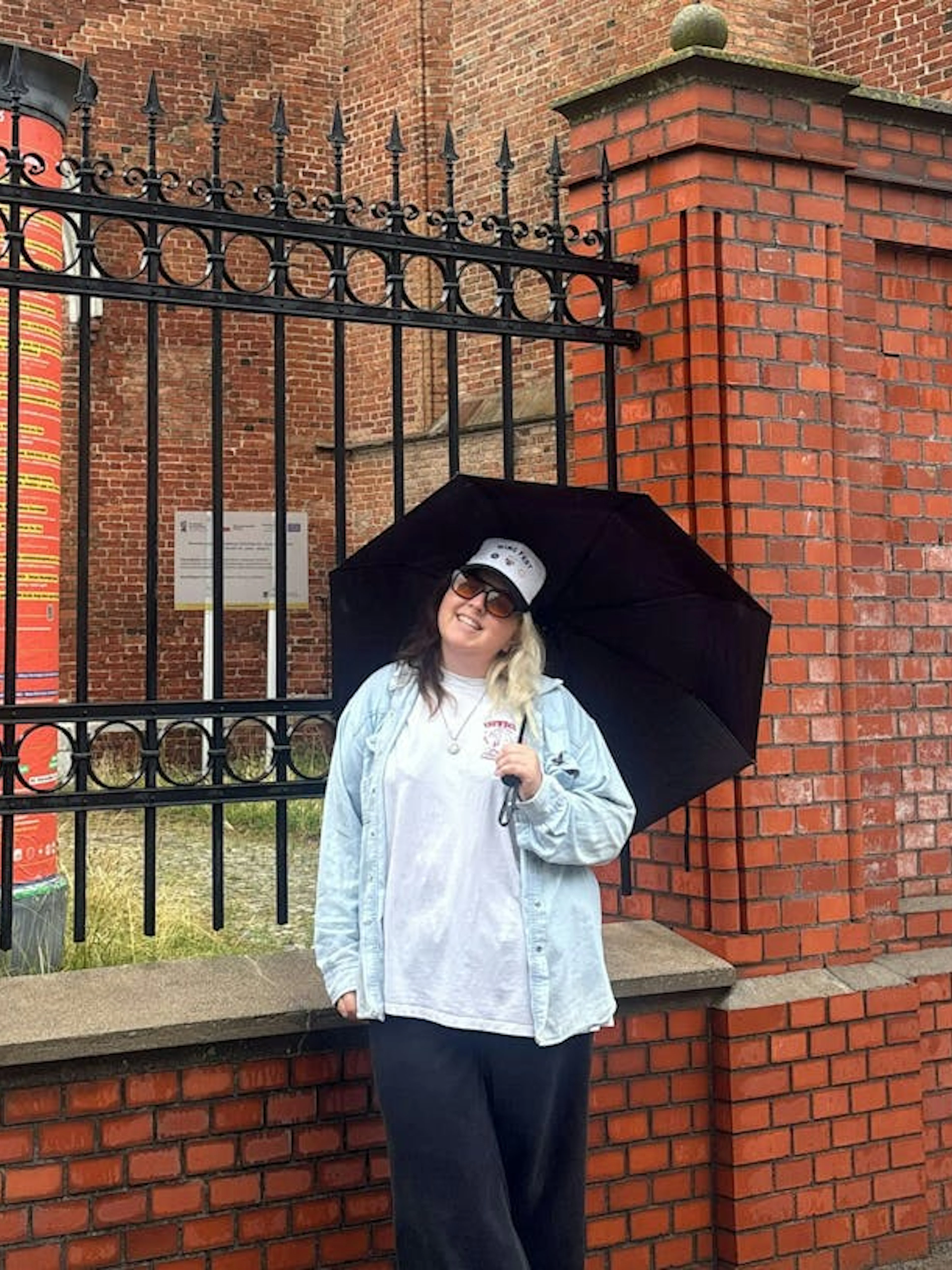 Person with umbrella near red brick wall in Gdansk during self-guided city exploration game.