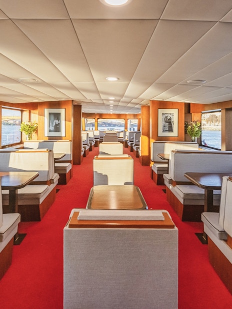 Interior of a sightseeing cruise with large windows and dining booths along a river.