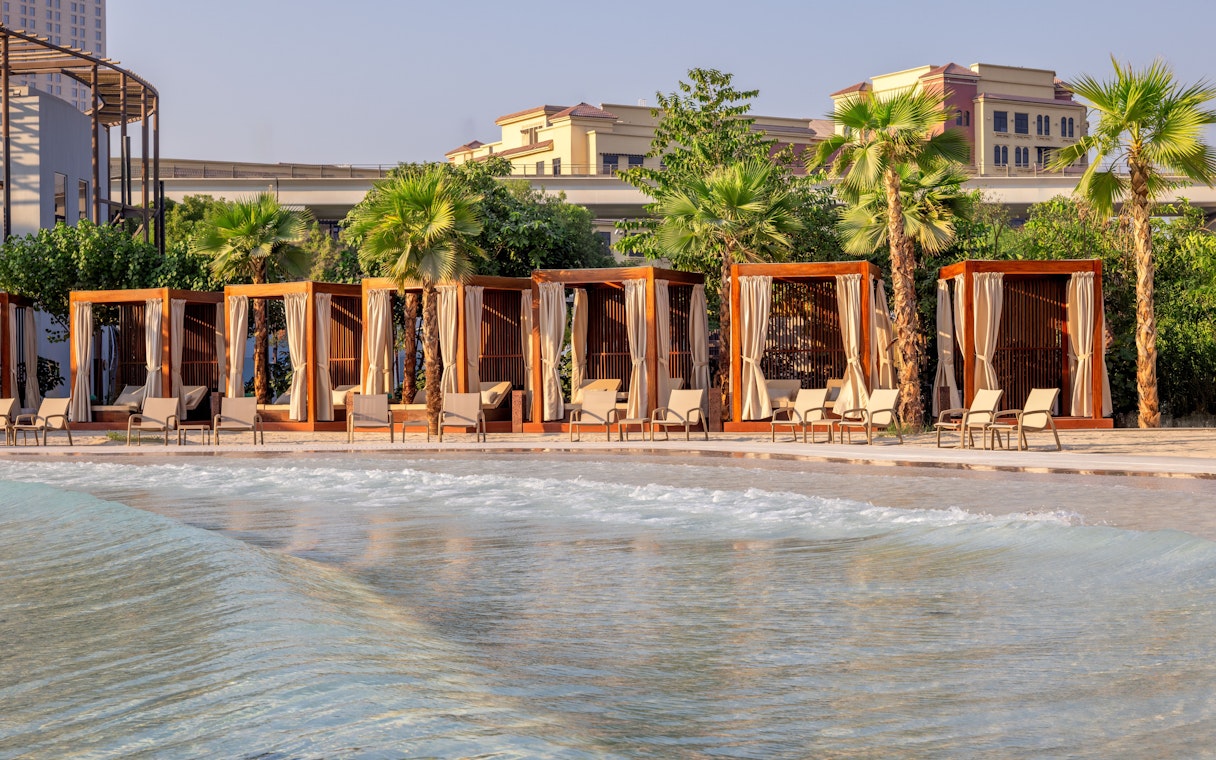 Lounge chairs by wave pool at Grand Hyatt waterpark, Dubai with cabanas and palm trees.