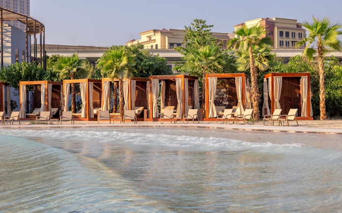 Lounge chairs by wave pool at Grand Hyatt waterpark, Dubai with cabanas and palm trees.