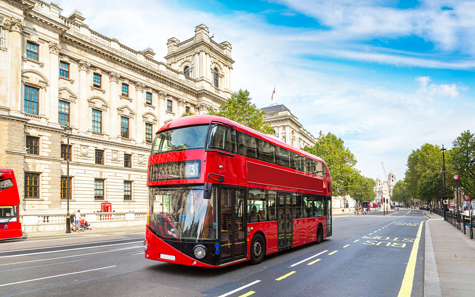 Red double-decker bus on a London street near historic buildings.