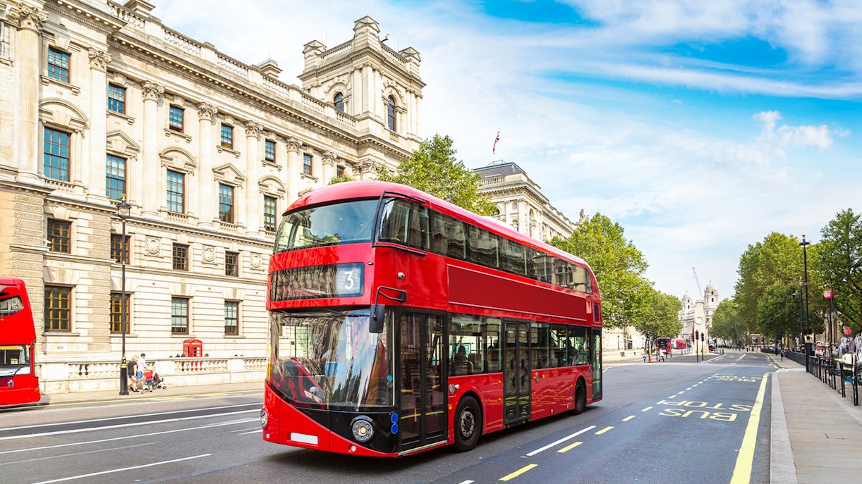 Red double-decker bus on a London street near historic buildings.