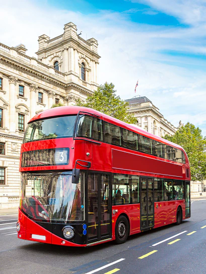 Red double-decker bus on a London street near historic buildings.