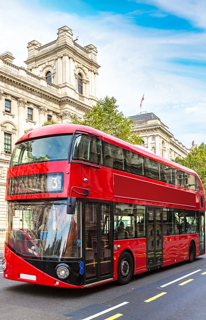 Red double-decker bus on a London street near historic buildings.