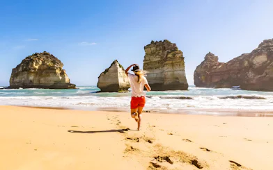 Lady running on beach near rock formations, Great Ocean Road, Australia.