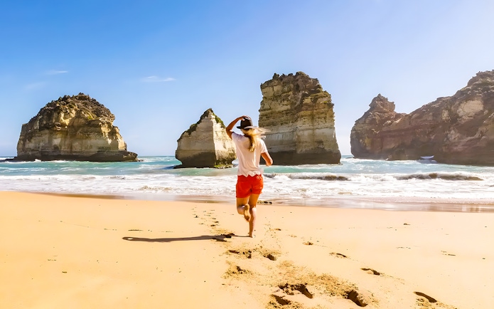 Lady running on beach near rock formations, Great Ocean Road, Australia.