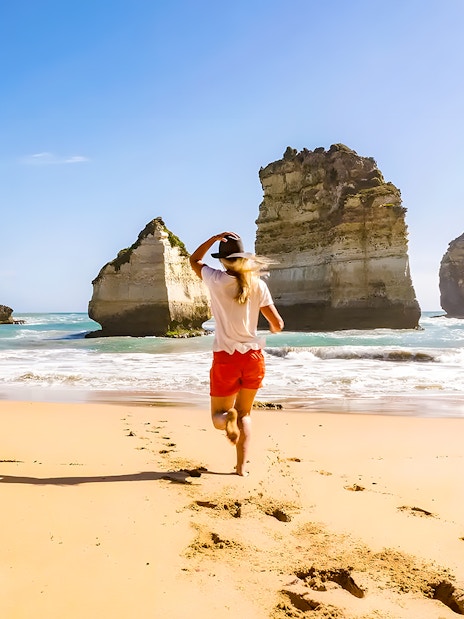 Lady running on beach near rock formations, Great Ocean Road, Australia.