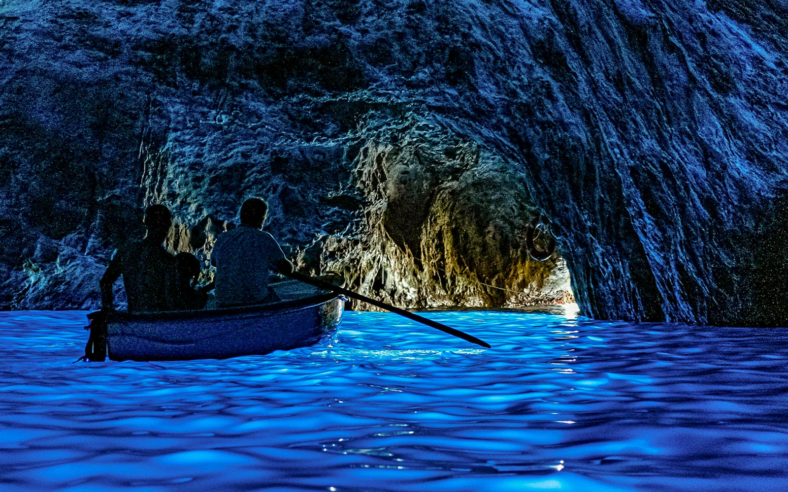 Boat entering Blue Grotto cave with glowing blue water, Capri.