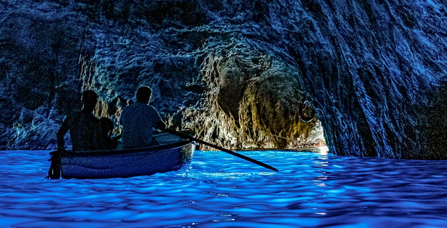 Boat entering Blue Grotto cave with glowing blue water, Capri.