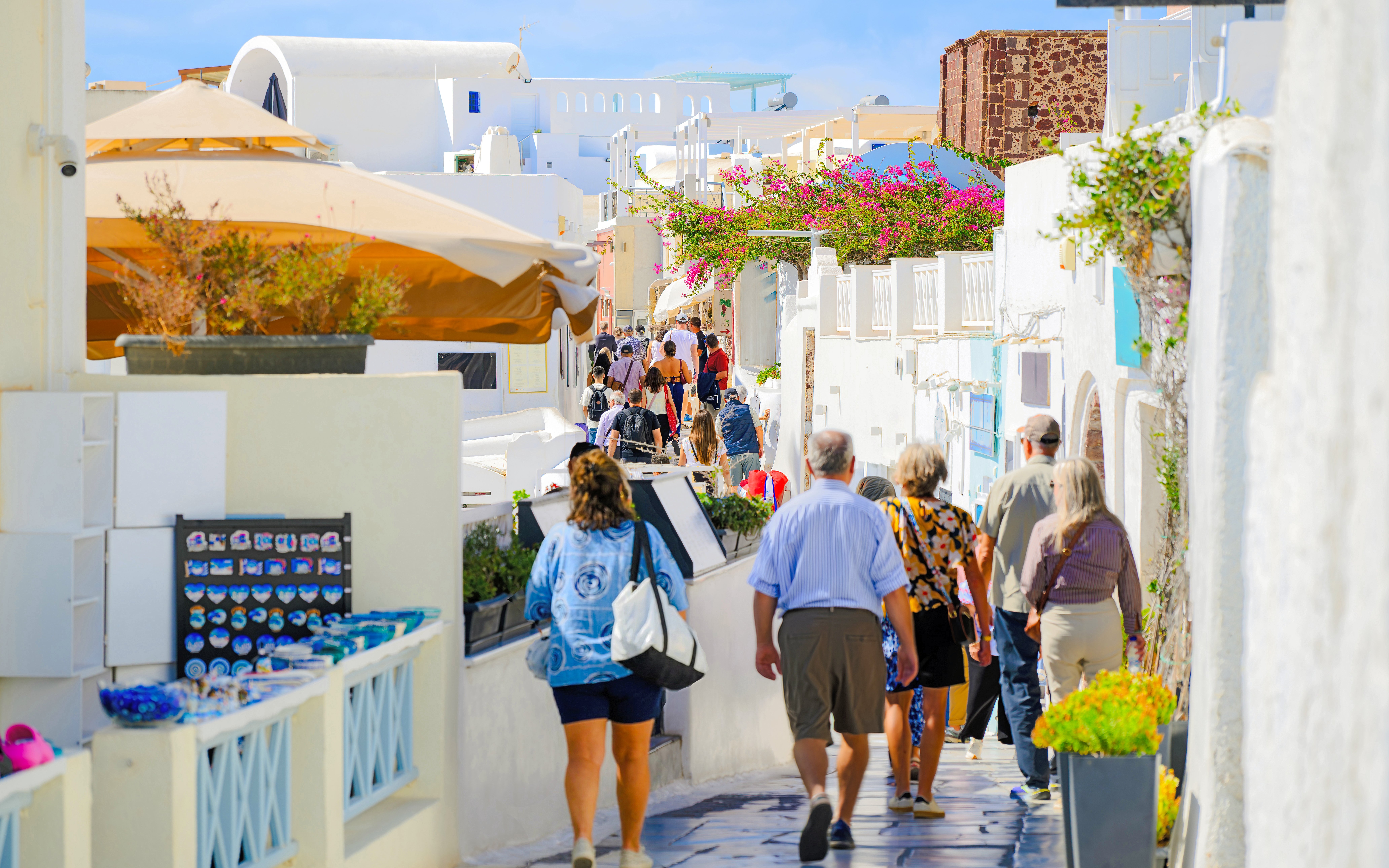 Pedestrian walkway in Fira old town, Santorini, with tourists exploring shops and whitewashed buildings.