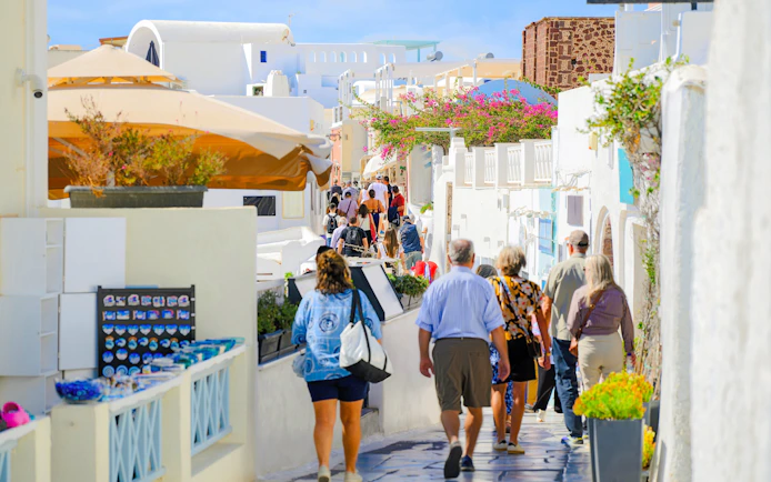 Pedestrian walkway in Fira old town, Santorini, with tourists exploring shops and whitewashed buildings.
