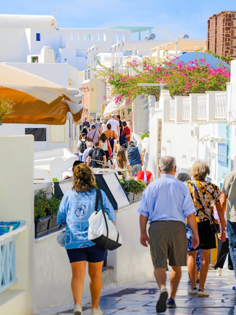 Pedestrian walkway in Fira old town, Santorini, with tourists exploring shops and whitewashed buildings.
