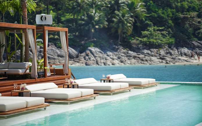 Sun loungers by the pool at Yona Beach Club, Phuket, with ocean and palm trees in the background.