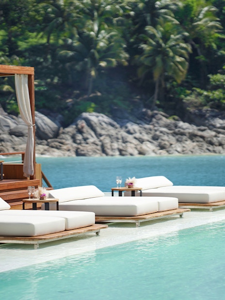 Sun loungers by the pool at Yona Beach Club, Phuket, with ocean and palm trees in the background.