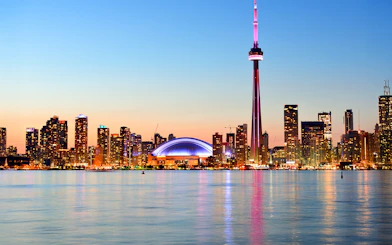 Toronto skyline with CN Tower at sunset reflecting on Lake Ontario.