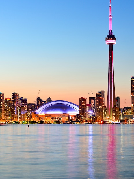 Toronto skyline with CN Tower at sunset reflecting on Lake Ontario.
