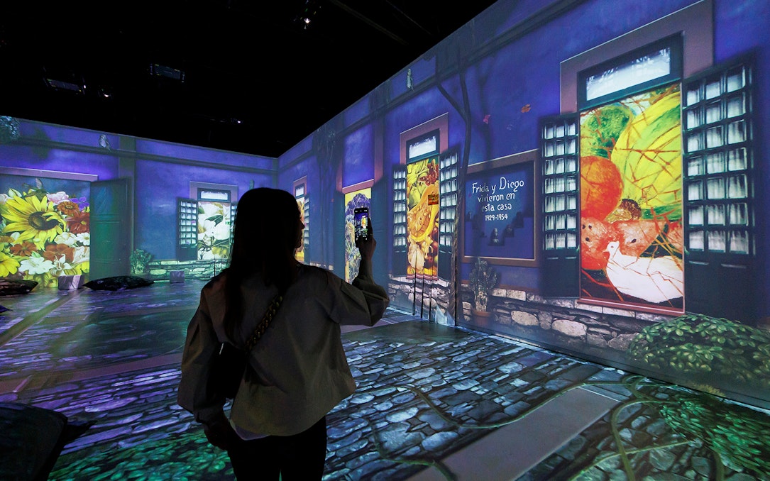 Frida Kahlo Immersive Exhibition with projected artwork and visitor taking photo.
