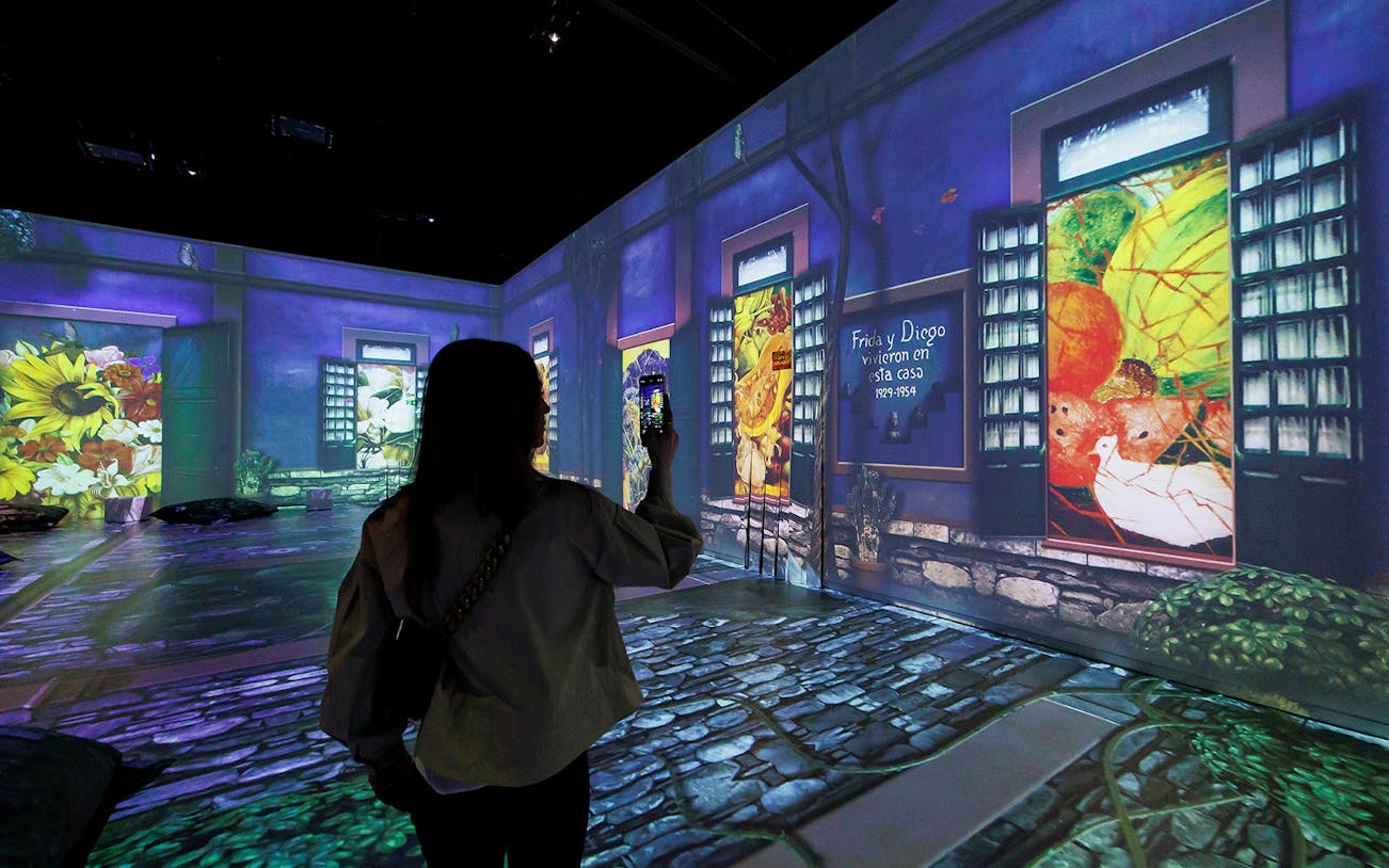 Frida Kahlo Immersive Exhibition with projected artwork and visitor taking photo.