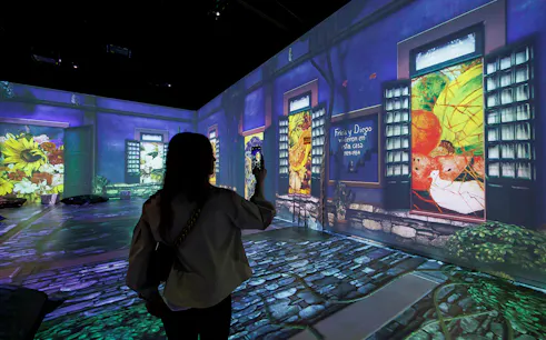 Frida Kahlo Immersive Exhibition with projected artwork and visitor taking photo.