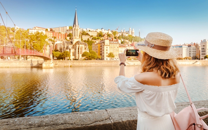 Woman photographing Lyon's Saône River and Saint George Church, France.
