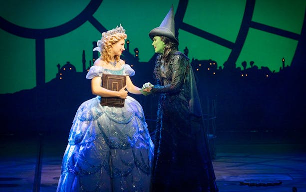 Two characters from Wicked musical on stage, one in a blue gown, the other in a black hat.