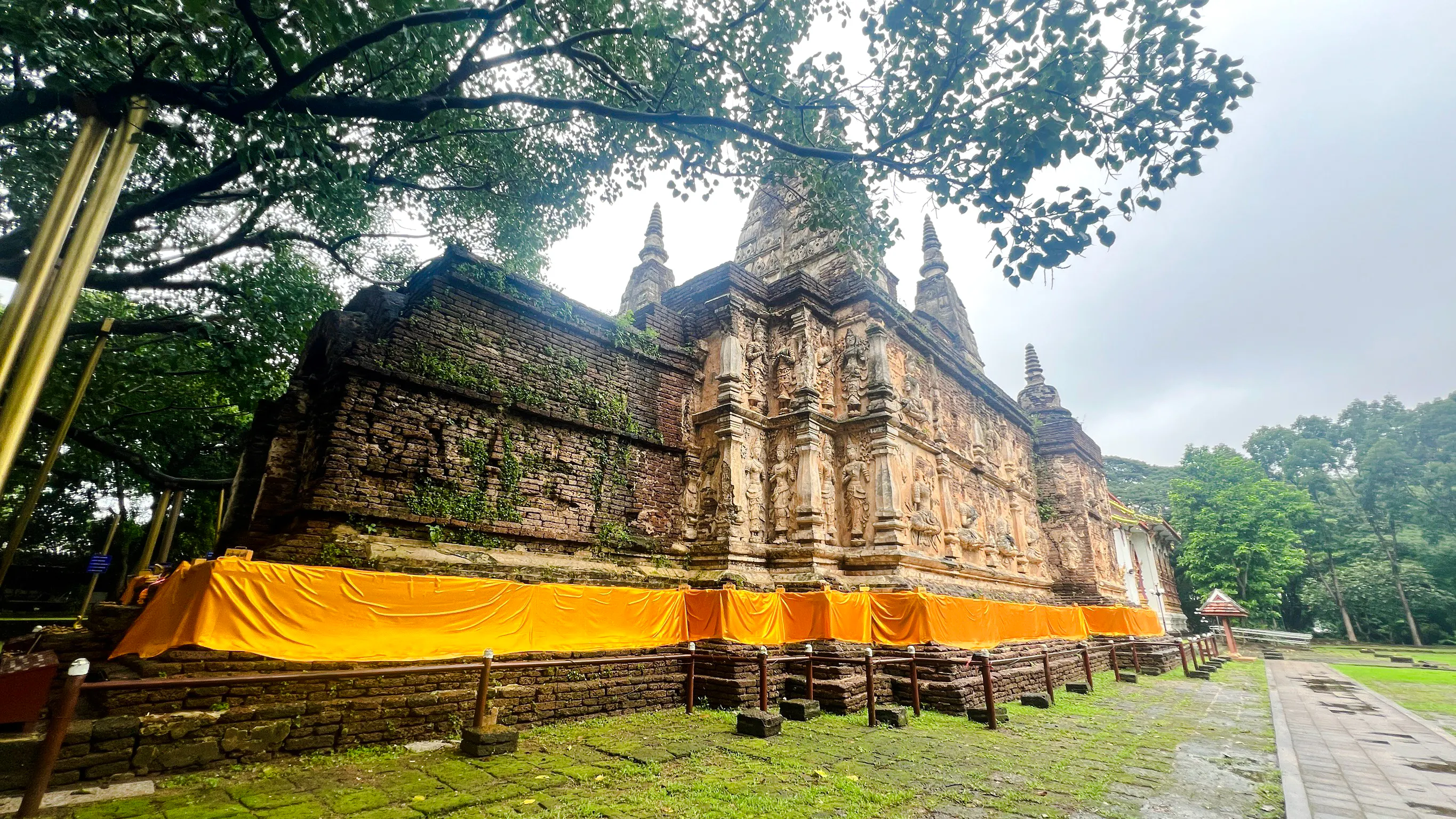 Ancient temple with intricate carvings and orange drapery in Chiang Mai, surrounded by lush greenery.
